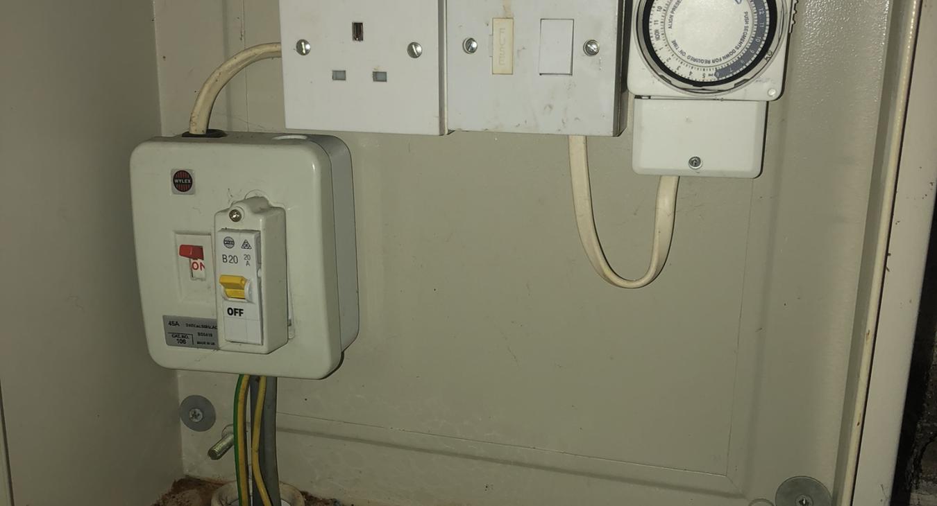 commercial electrician looks at LED floodlight timer and distribution board with water ingress in Rochester