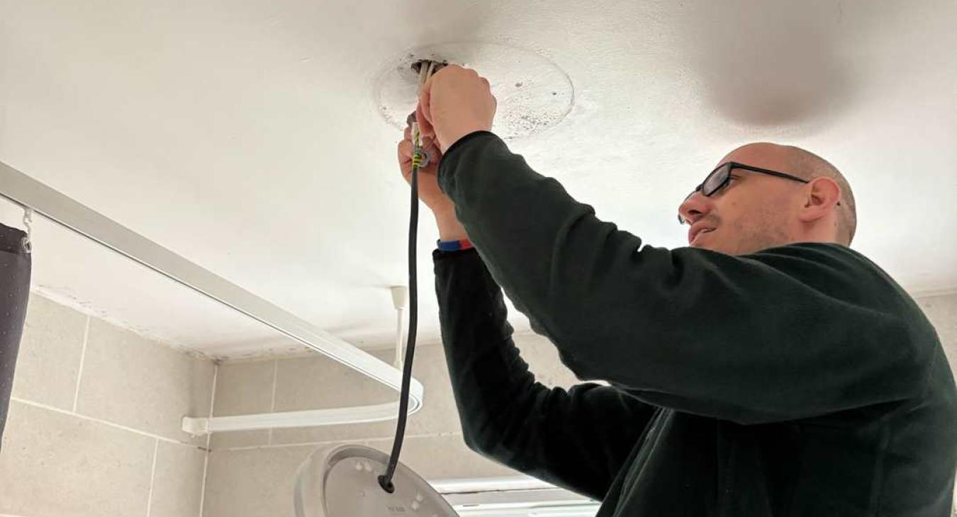 Registered electrician changing bathroom light as part of small job service